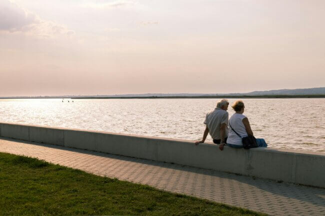 Two elderly people sitting by the sea enjoying life.
