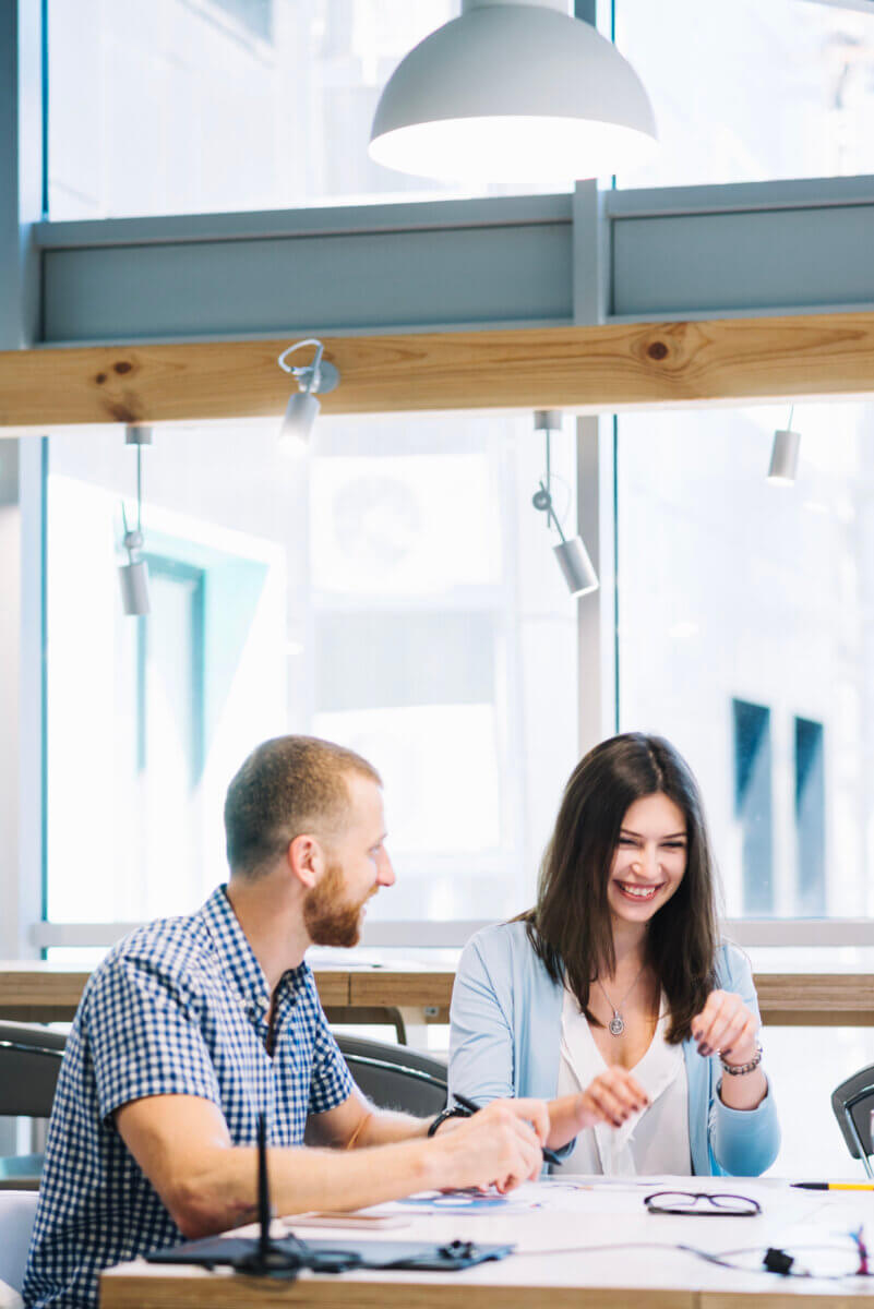 two colleagues sitting at a desk talking and smiling