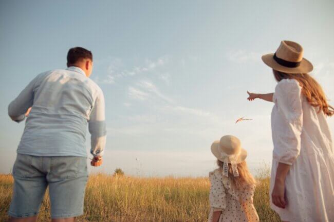 a family of two adults and a child looking on to a field of hay and the blue sky