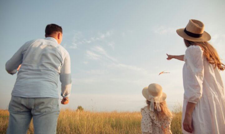 a family of two adults and a child looking on to a field of hay and the blue sky