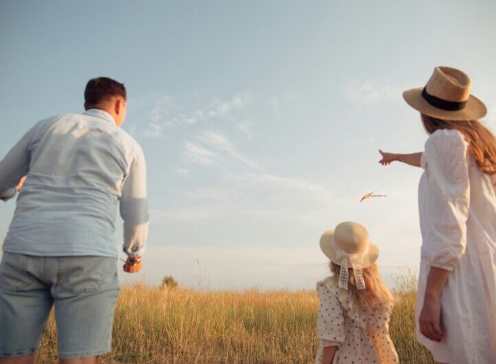 a family of two adults and a child looking on to a field of hay and the blue sky