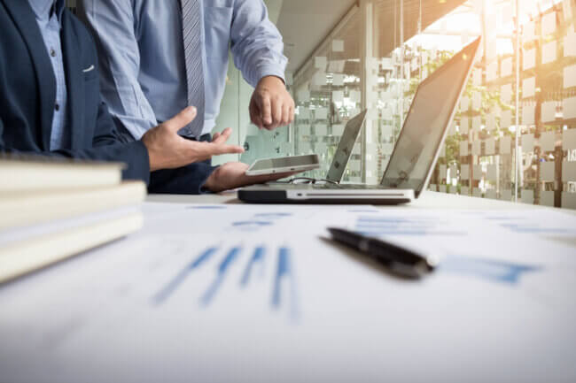 business analasing progress, with two persons standing over laptop.