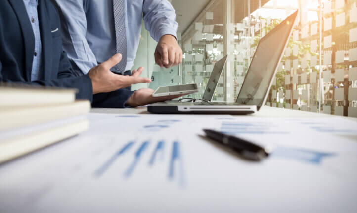 business analasing progress, with two persons standing over laptop.