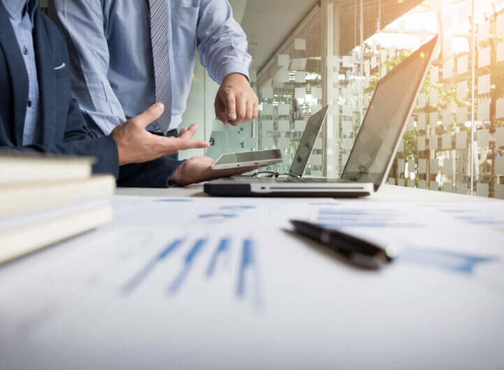 business analasing progress, with two persons standing over laptop.