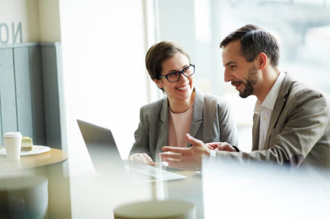 Two business people sitting by laptop discussing business