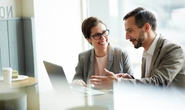 Two business people sitting by laptop discussing business