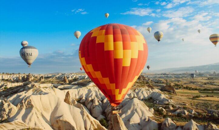 Orange and yellow balloon going up the landscape of Turkey, with blue skies in the background.