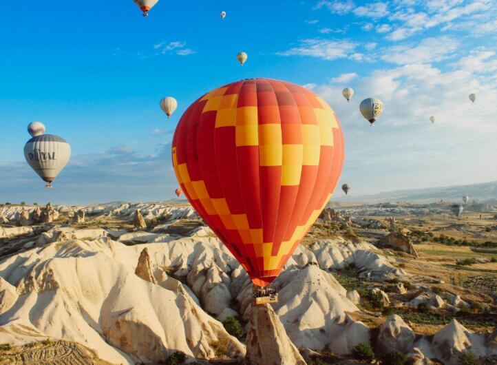 Orange and yellow balloon going up the landscape of Turkey, with blue skies in the background.
